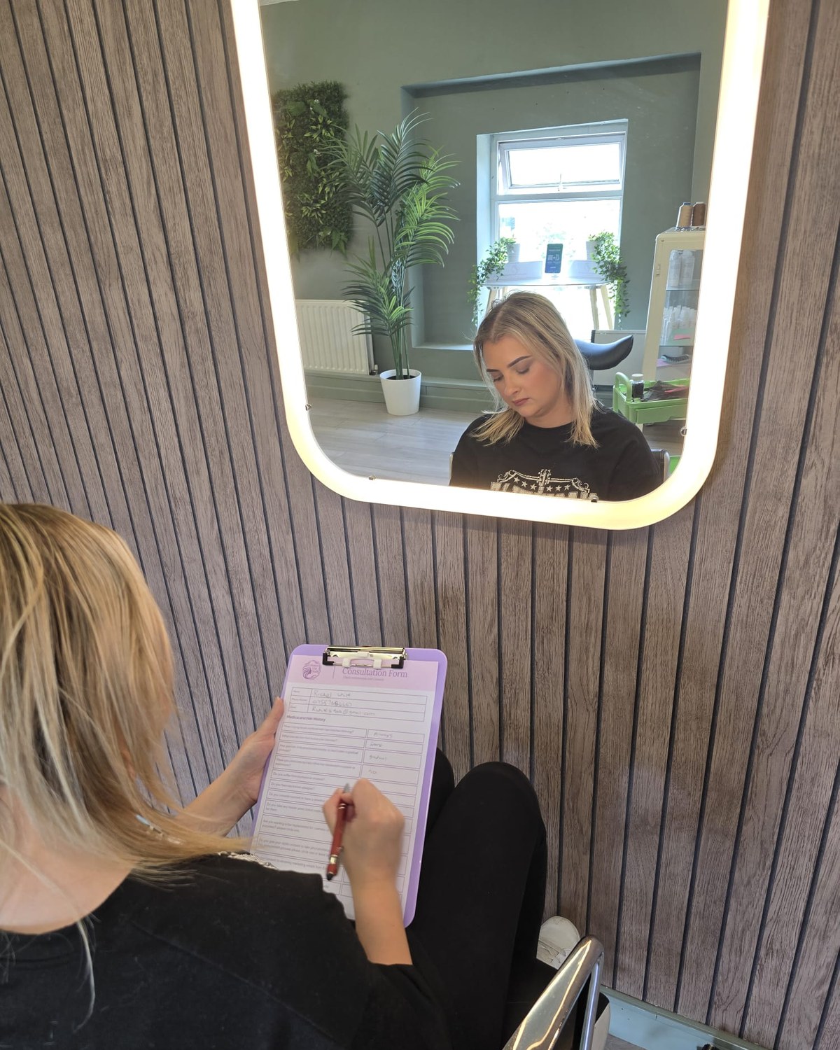 A client completing her private consultation form at Enhanced Hair Studio, reflected in the salon mirror